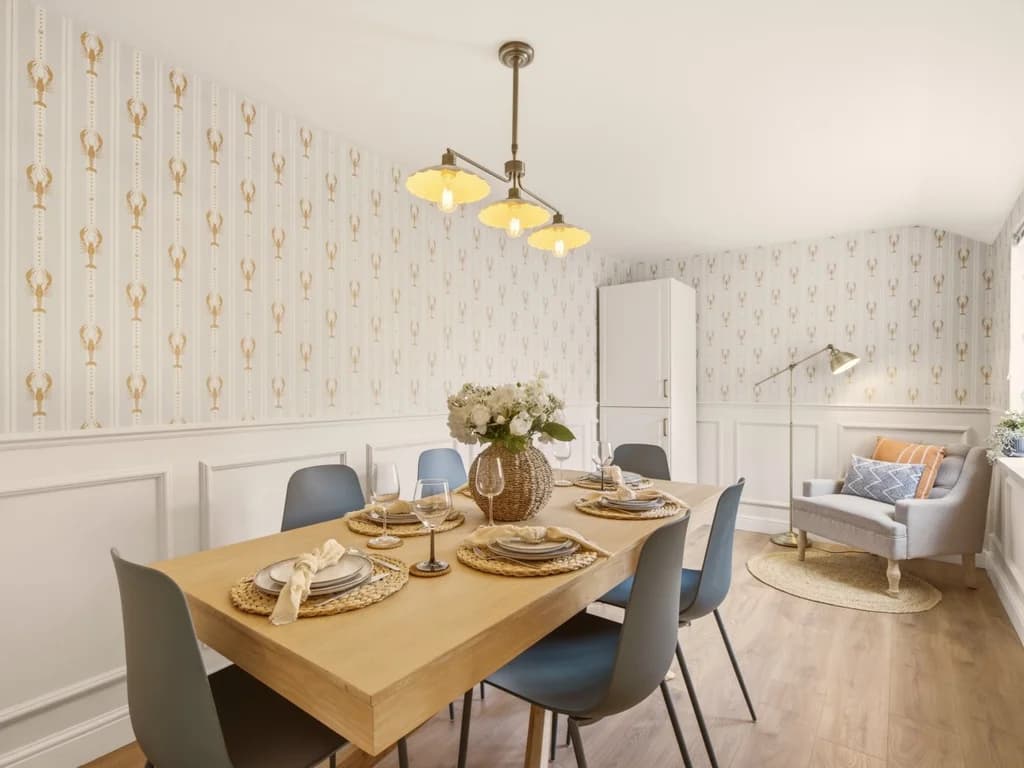 Dining room with patterned wallpaper and four-seat wooden table.
