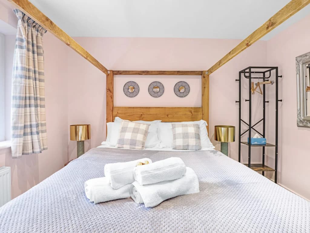 This bedroom features a rustic wooden four-poster bed accented by plaid pillows, gold bedside lamps, and a modern open wardrobe.