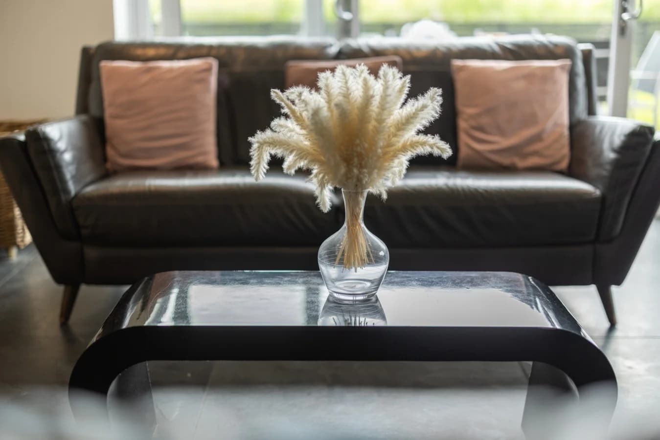 Glass coffee table with dried pampas arrangement before leather sofa