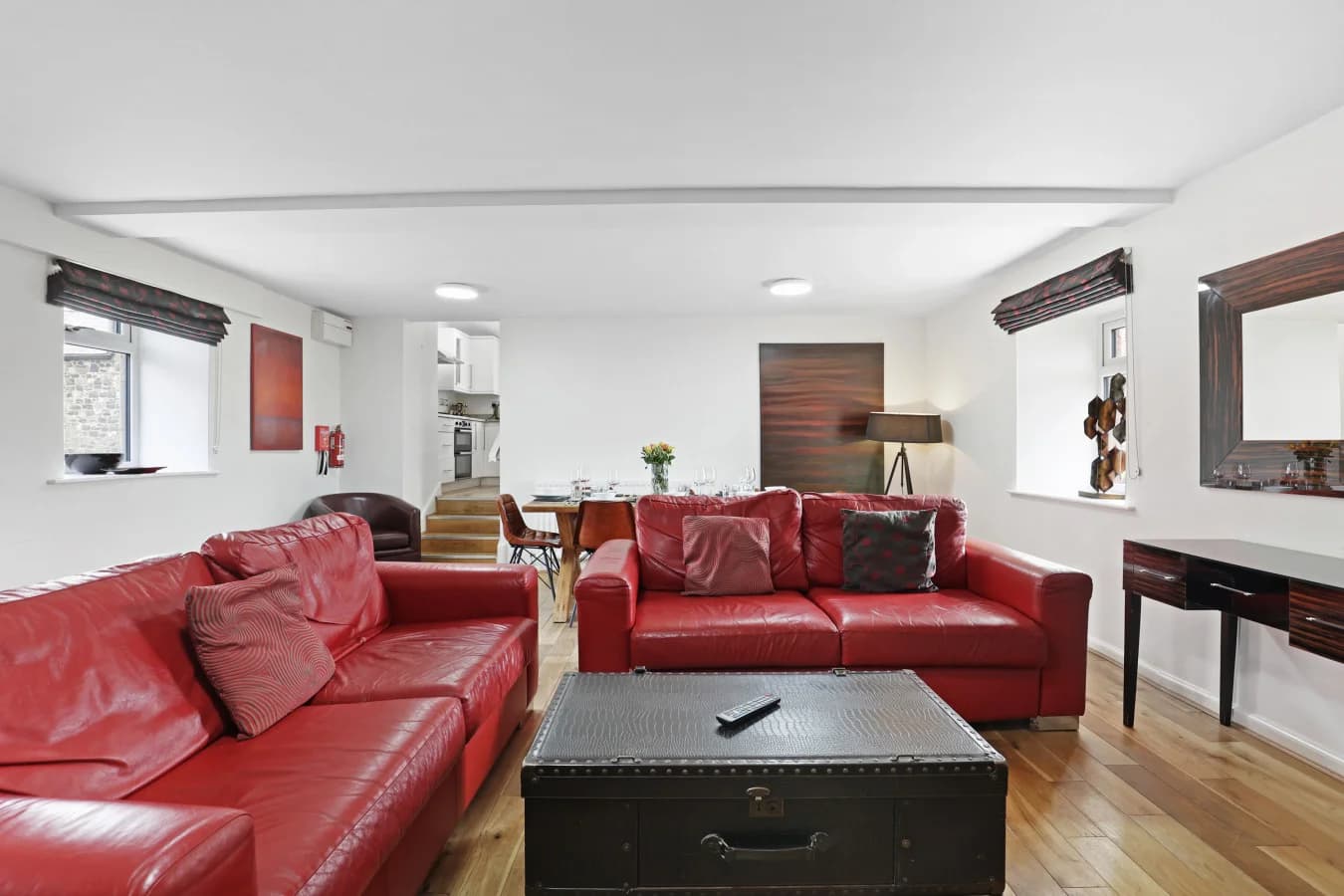 Open-plan living area with red leather seating and oak flooring.