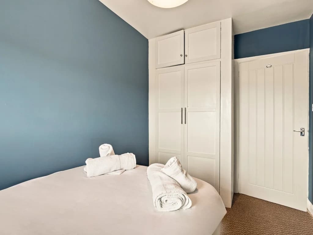 Small double bedroom with fitted wardrobe and blue feature wall.