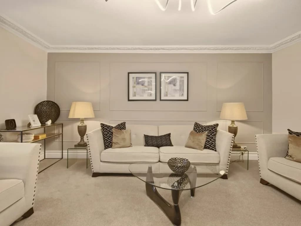 Spacious living room with cream seating, glass table and panelled walls.