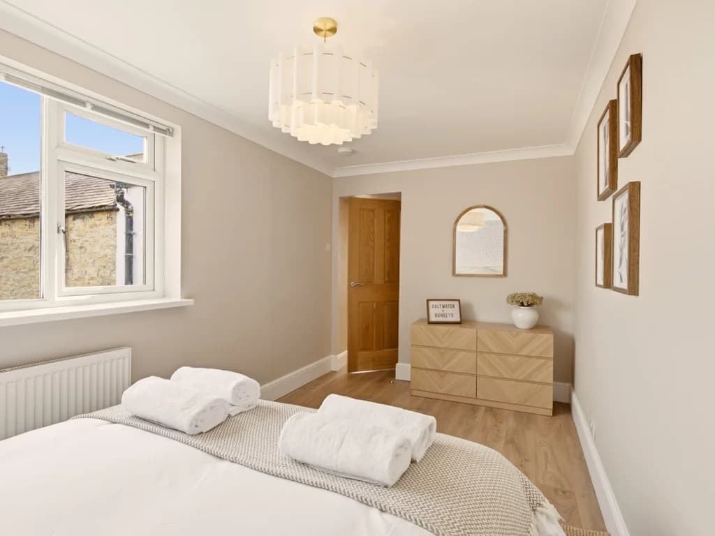 Bright king bedroom with large windows and wooden chest of drawers