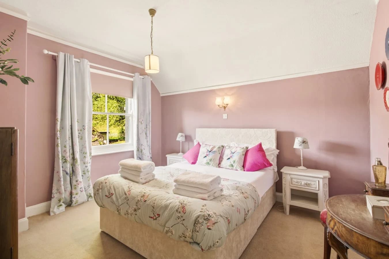 Pink bedroom with upholstered double bed, dressing table and garden view