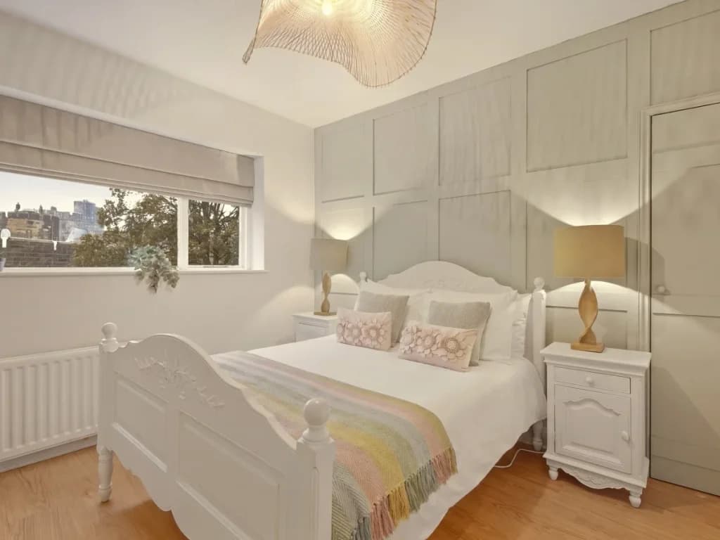 Bright double bedroom with panelled walls and traditional white furniture.
