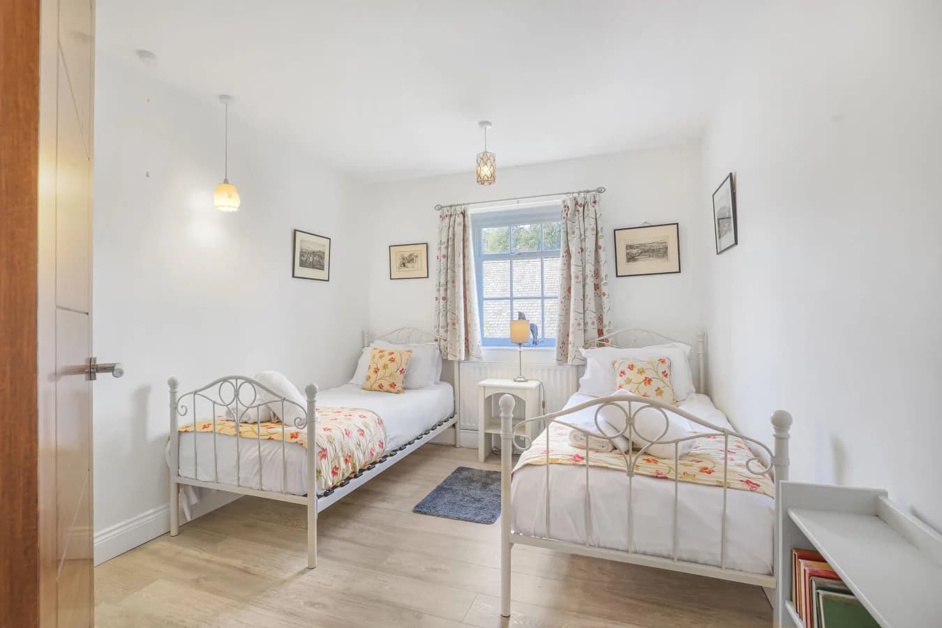 Twin bedroom with cream metal bedframes and garden-facing window