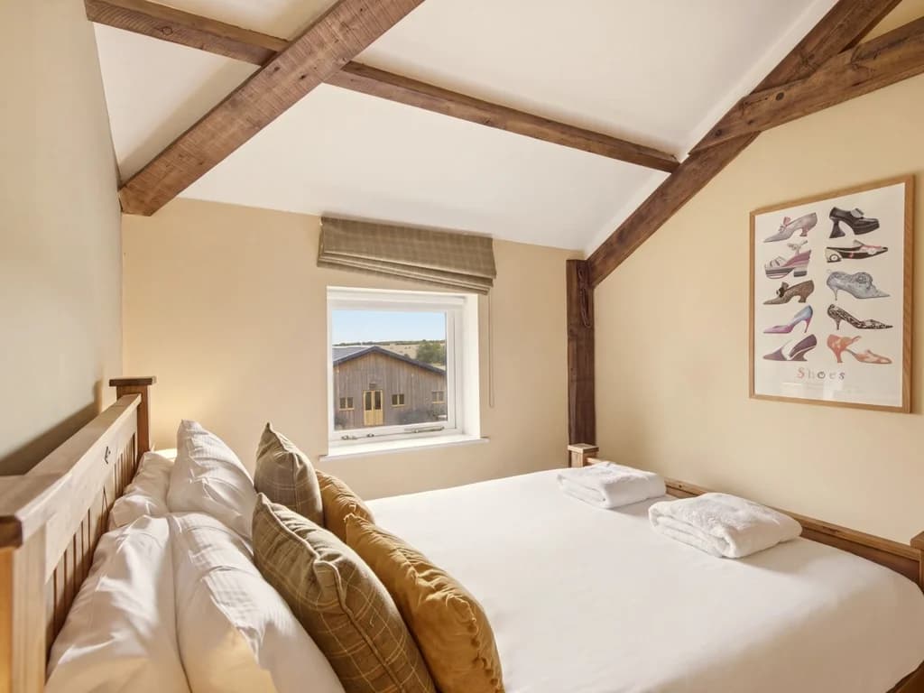 King-size bed beneath exposed beams with countryside views from window