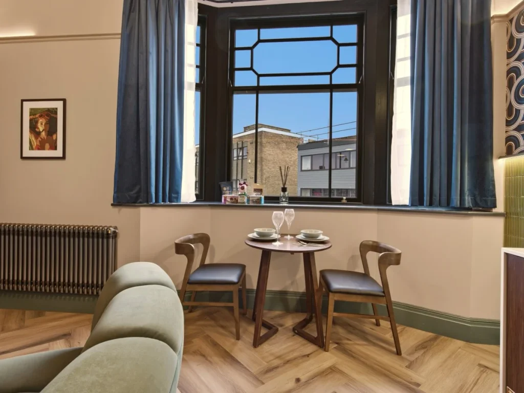Dining area set for two beside the large bay window and kitchen.