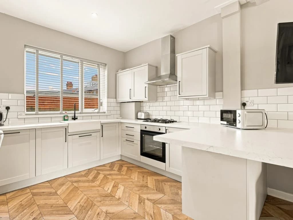 Bright fitted kitchen with breakfast bar and herringbone flooring.