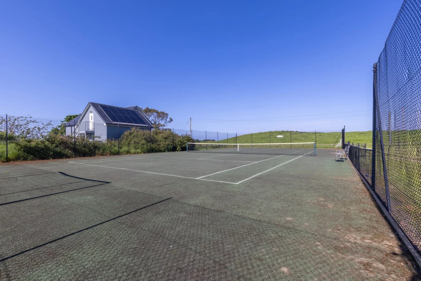 Fenced tennis court with open countryside surroundings
