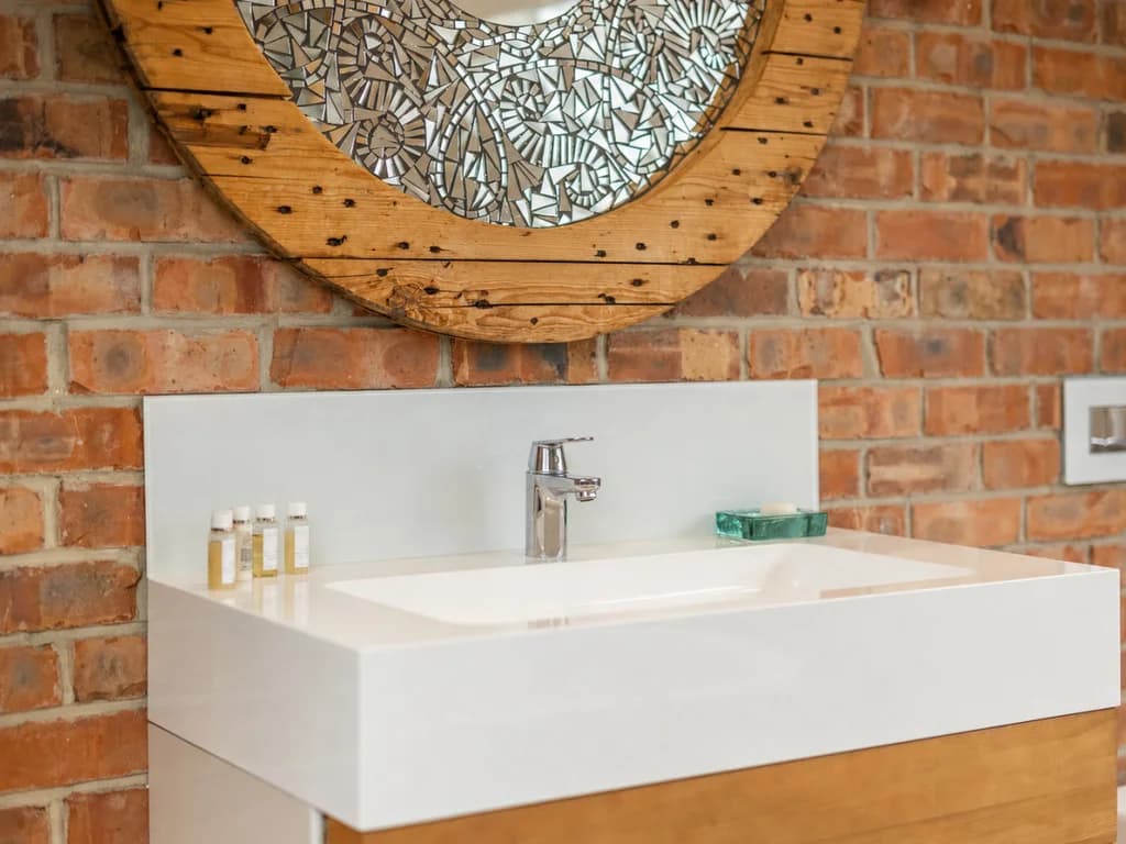 En-suite basin with reclaimed mosaic mirror on exposed brick wall.