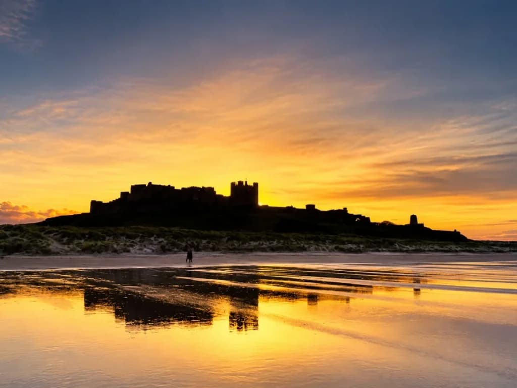 Bamburgh Castle silhouetted against a colourful coastal sunset