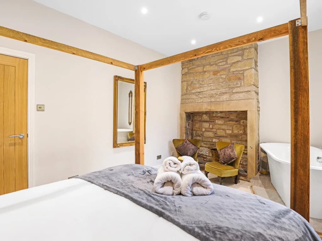 This luxurious bedroom features a wooden four-poster bed and a freestanding bathtub set against a rustic stone fireplace.