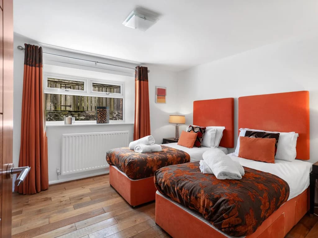 Twin bedroom with orange headboards and garden-facing window