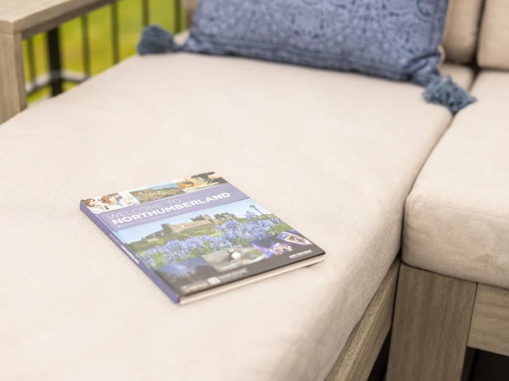 A travel guide titled "Welcome to Northumberland" rests on the beige cushion of an outdoor lounge sofa.