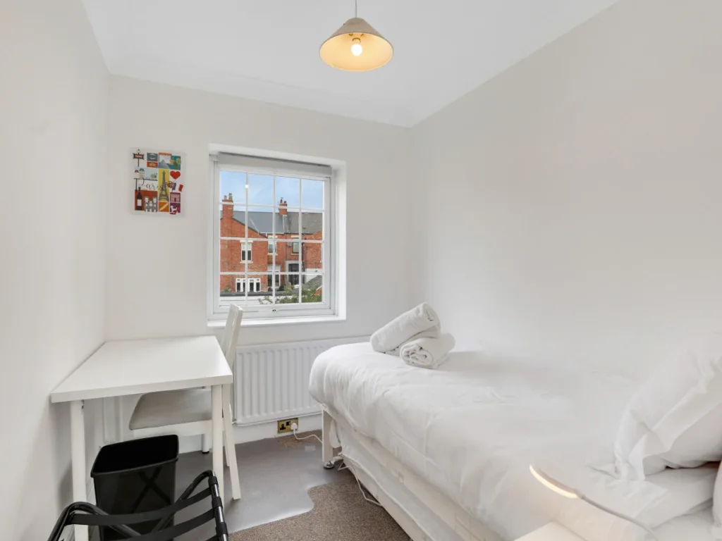 Single bedroom with desk, chair, window and fresh white bedding