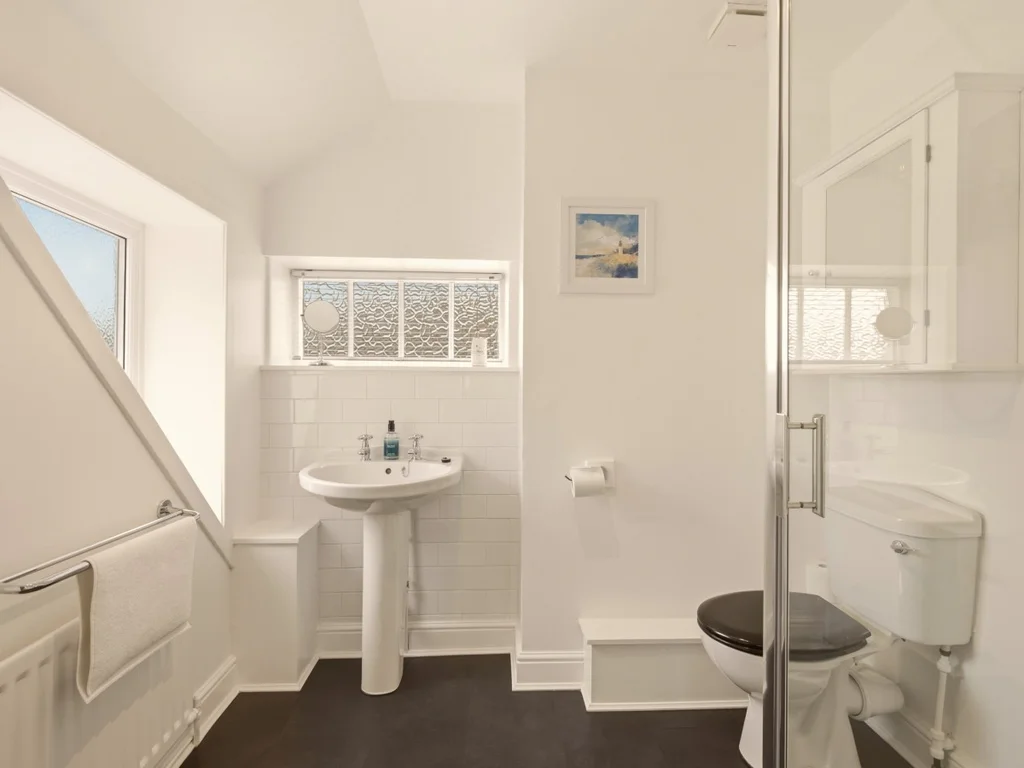 Bright en-suite bathroom with shower enclosure, pedestal basin and natural daylight