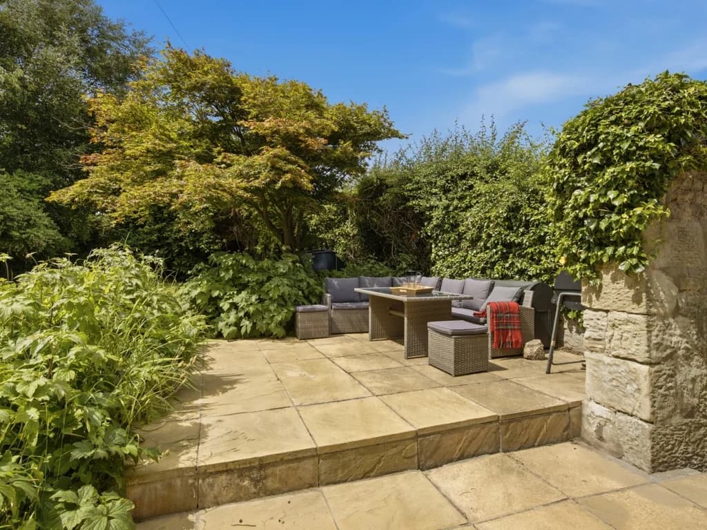 Private stone patio with outdoor seating surrounded by mature cottage gardens