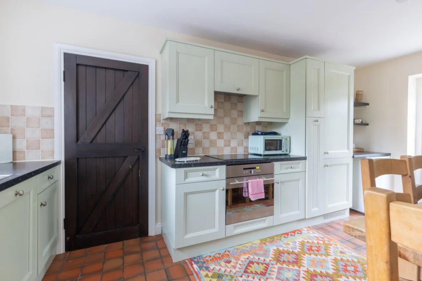 Country-style kitchen with sage cabinetry and patterned tile splashback