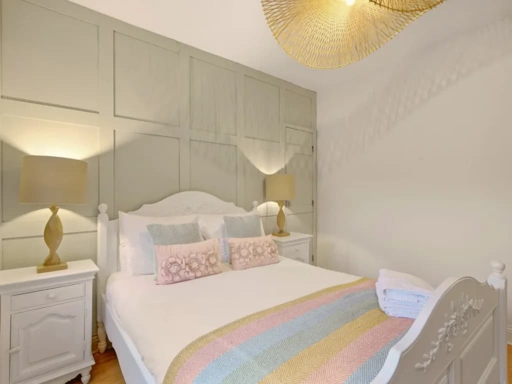 Traditional double bed with pastel throw, soft lighting and wood flooring.