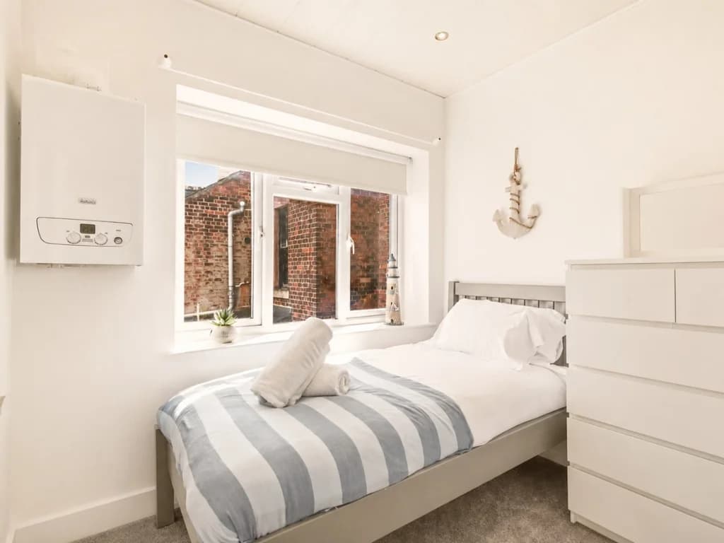 Single bedroom with chest of drawers and large window.