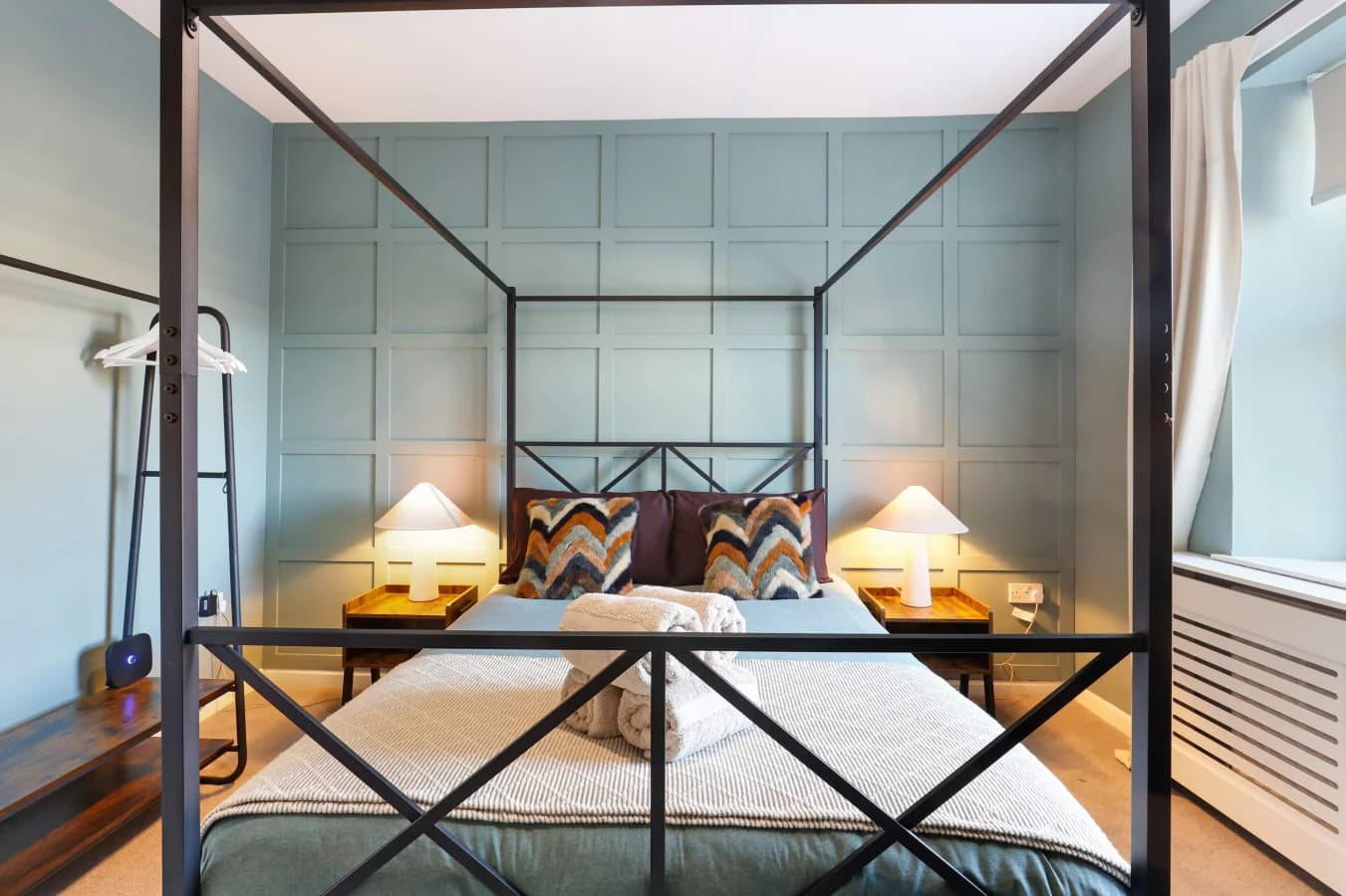 Statement four-poster bed framed by bespoke wall panelling and warm lighting