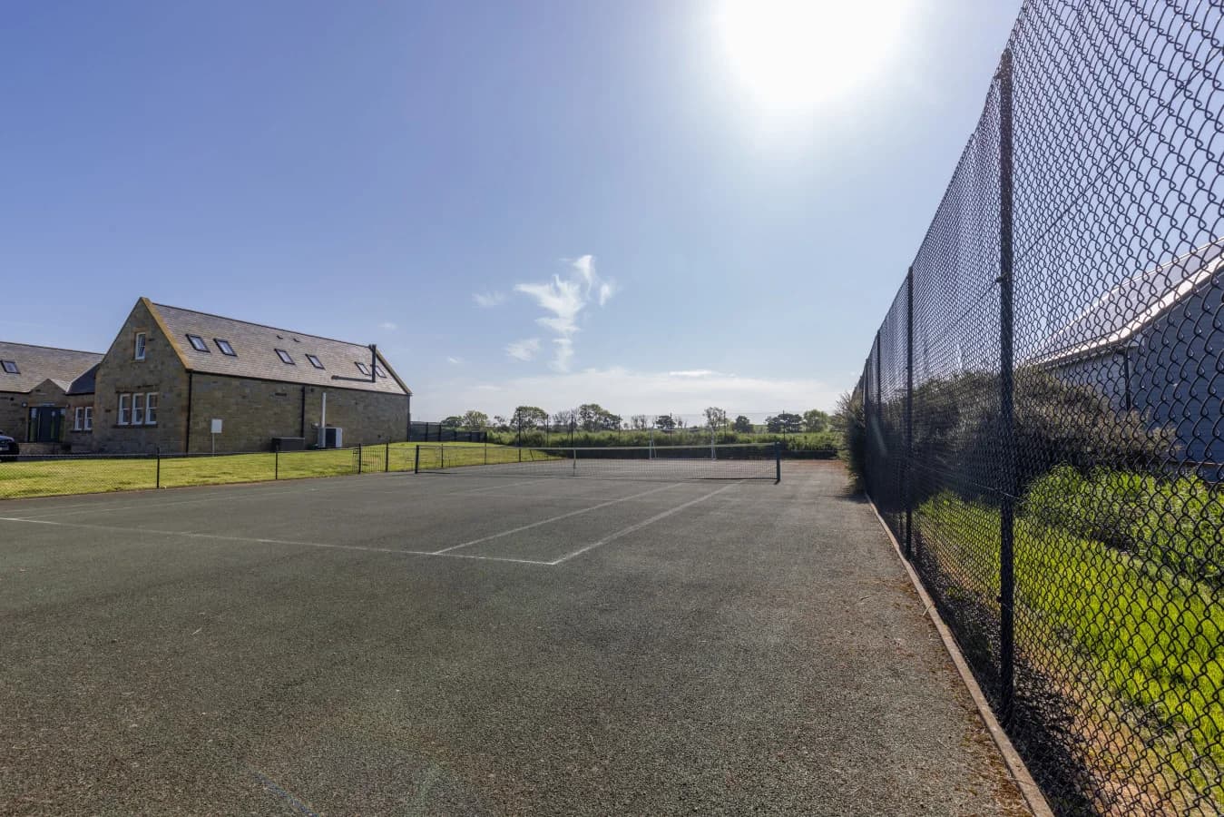 Tennis court beside traditional stone buildings and paddocks