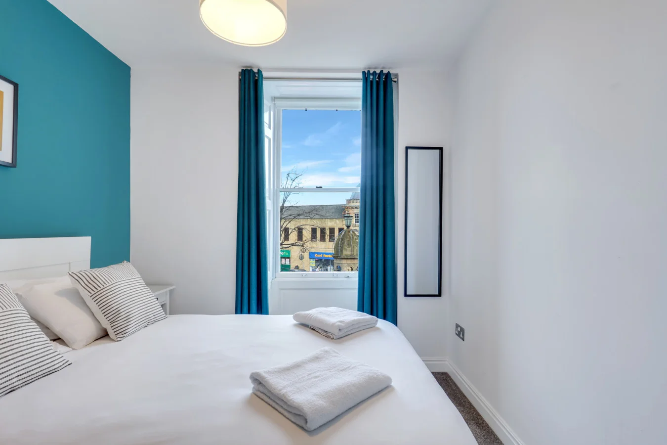 Bright double bedroom with a teal feature wall and elevated town views
