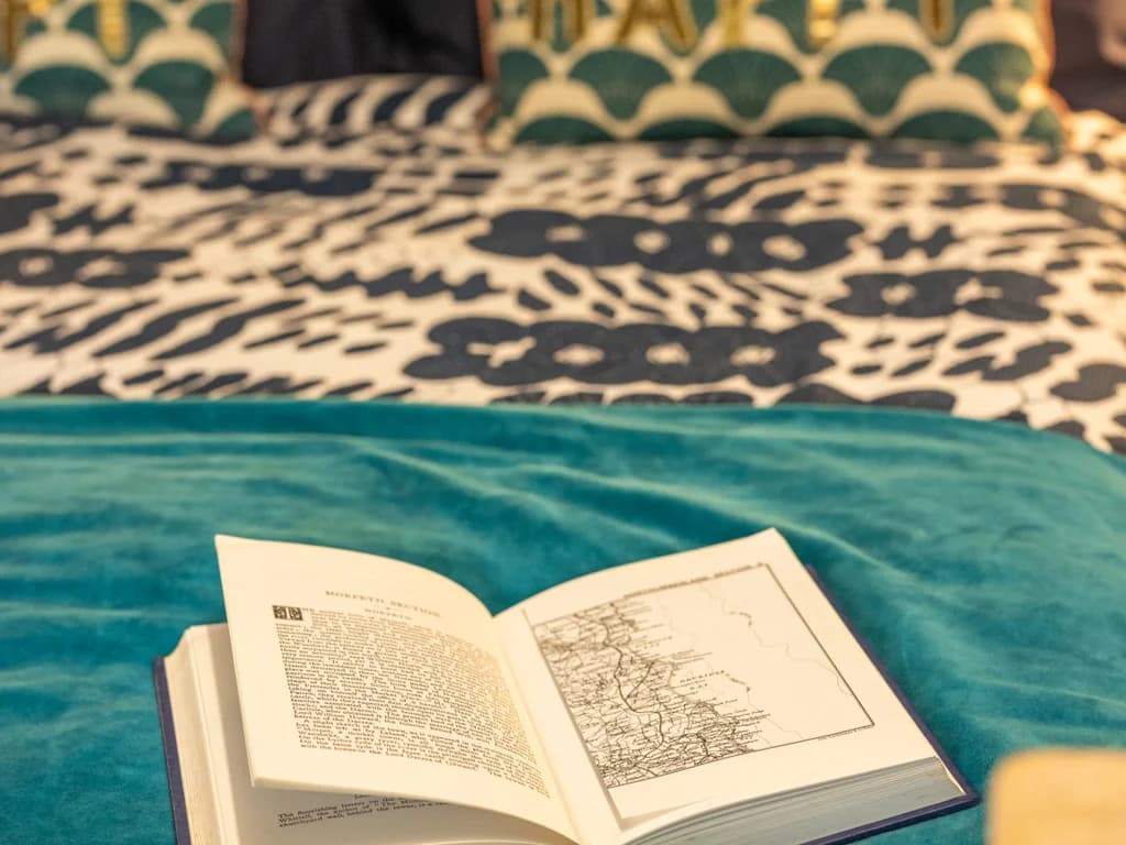 An open book featuring a map rests on a teal velvet throw.