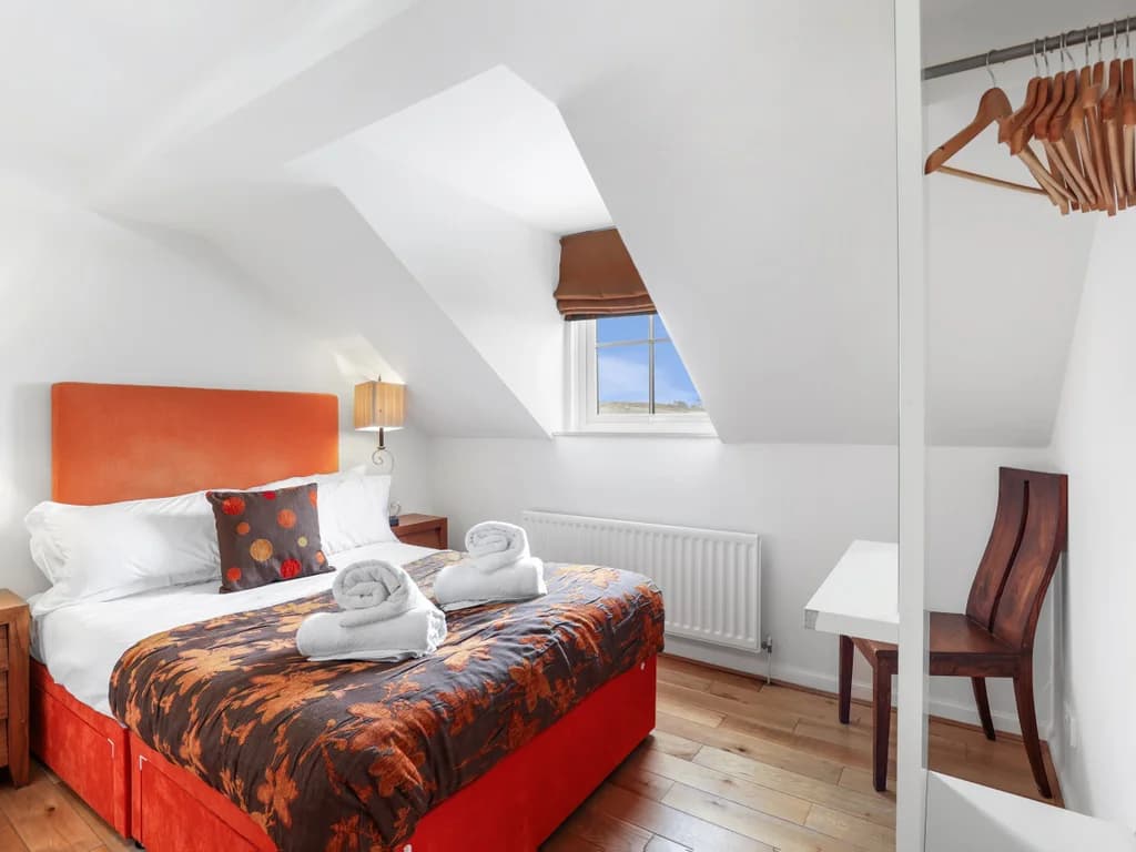 Double bedroom with orange upholstered bed beneath vaulted ceilings