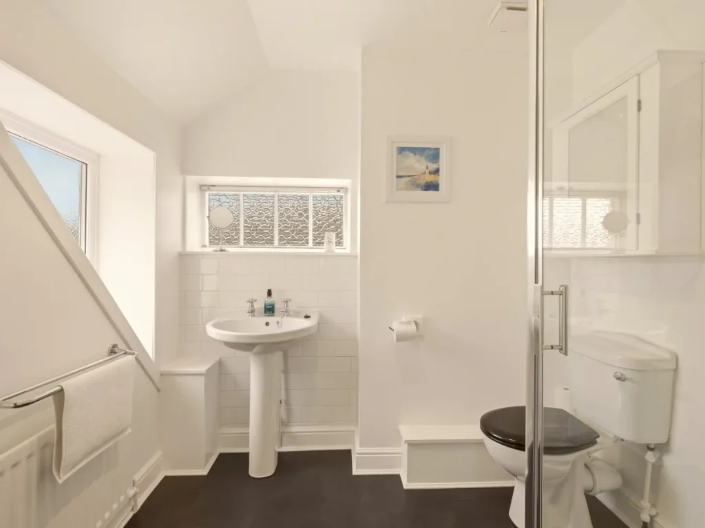 Bright en-suite bathroom with shower enclosure, pedestal basin and natural daylight