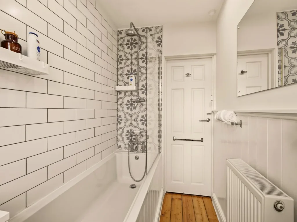 Family bathroom with tiled bath surround, shower fittings and large mirror