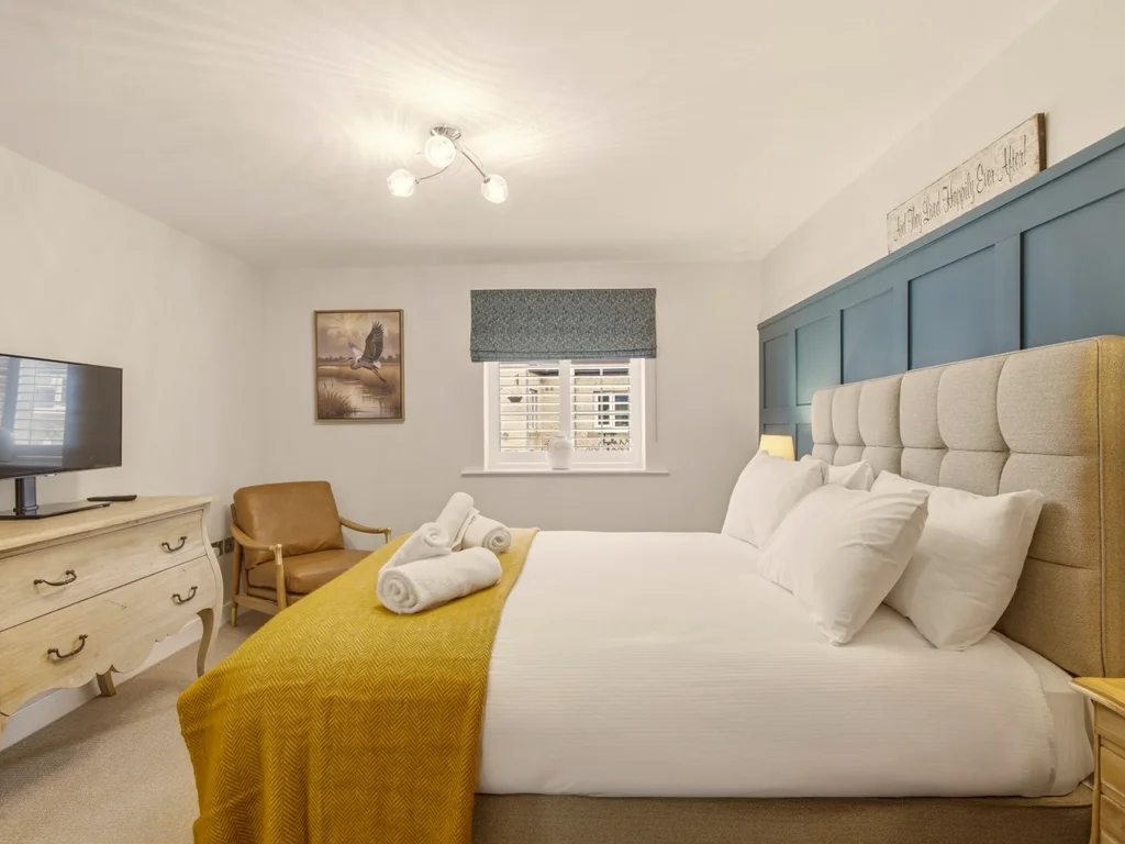 Elegant king bedroom with Smart TV, feature wall and comfortable armchair