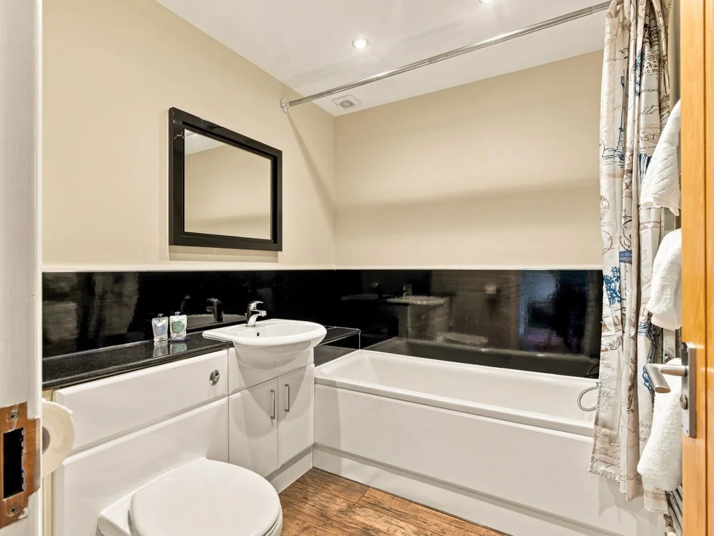 Family bathroom with bath, overhead shower and black feature tiles.