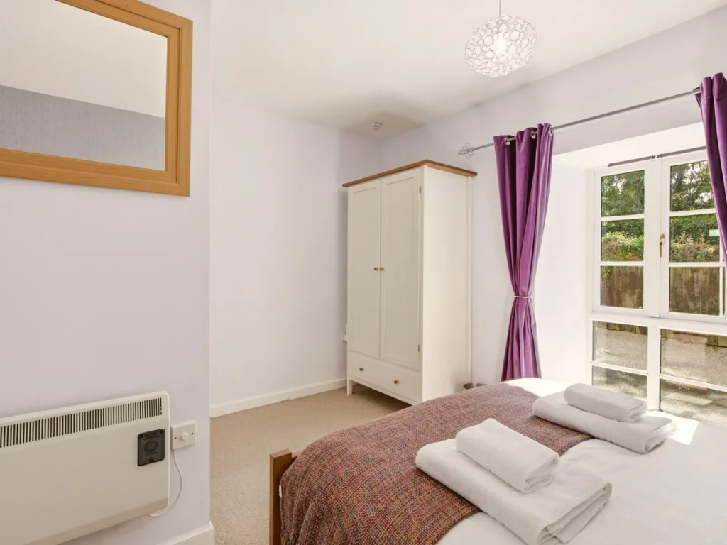 King bedroom with wardrobe, large mirror and doors overlooking greenery