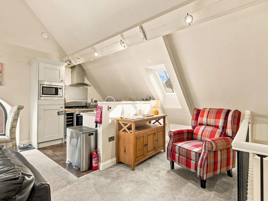 Comfortable lounge with tartan armchair and well-equipped kitchen beyond.