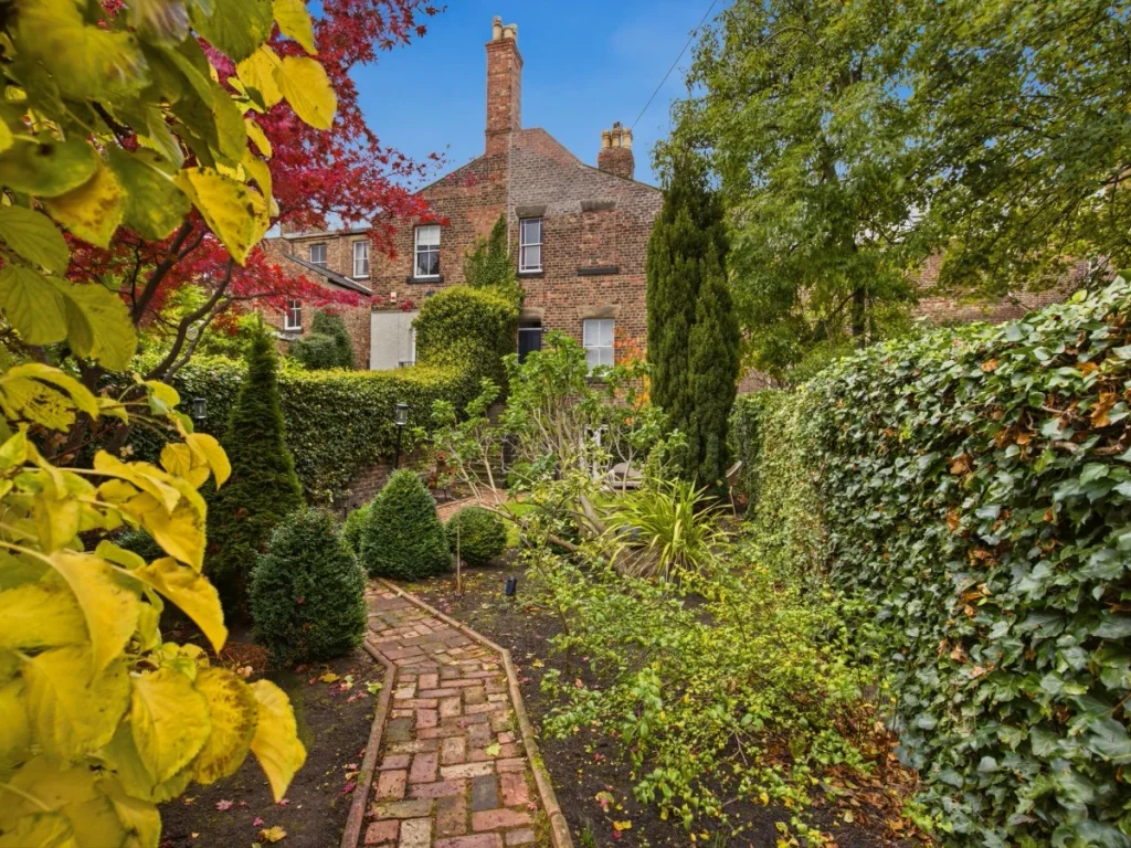Garden pathway bordered by colourful plants and mature hedges
