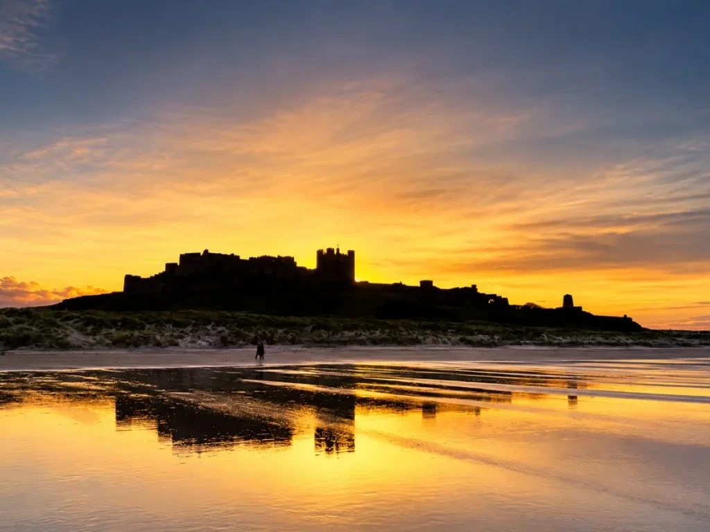 Bamburgh Castle silhouetted against a colourful coastal sunset