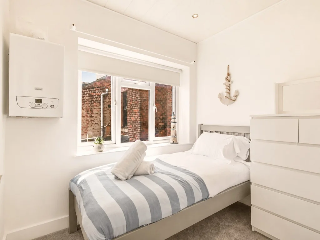 Single bedroom with chest of drawers and large window.