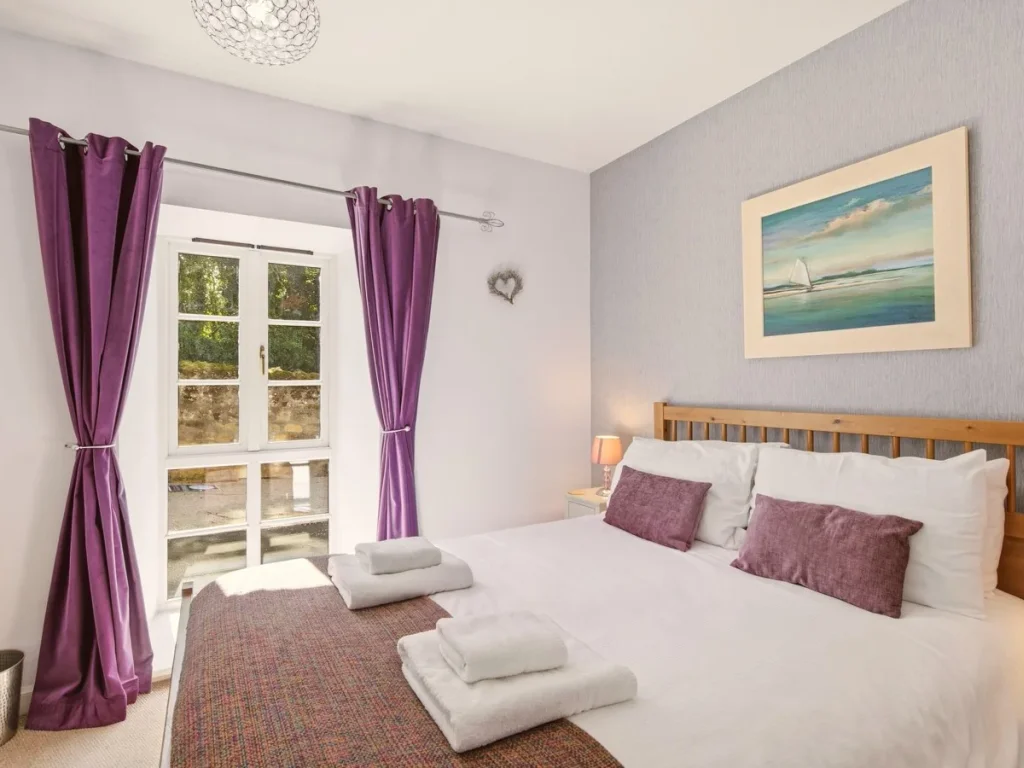 King bedroom with purple accents, bedside lighting and outdoor outlook