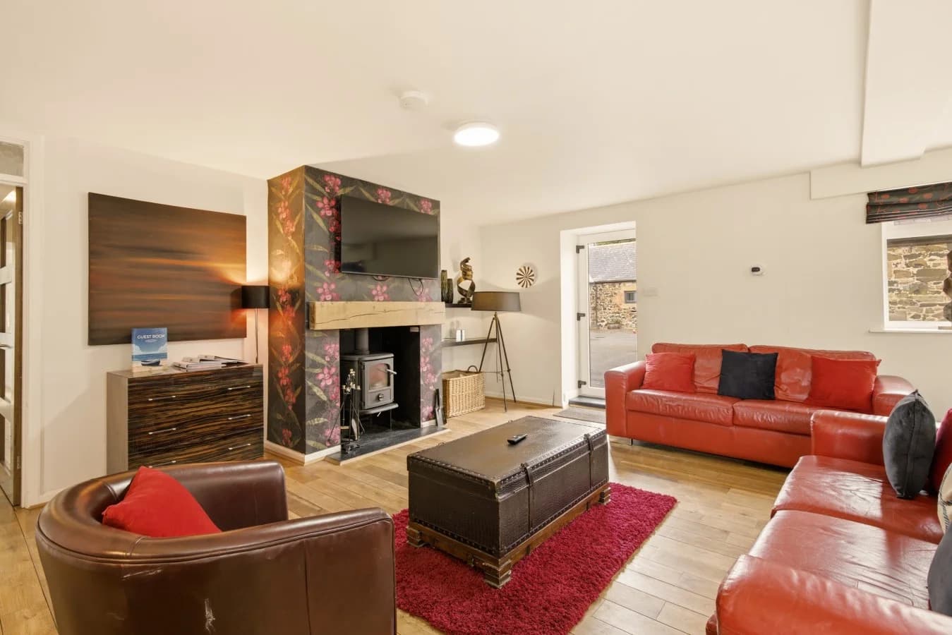 Open-plan lounge with red leather sofas, log burner and Smart TV.