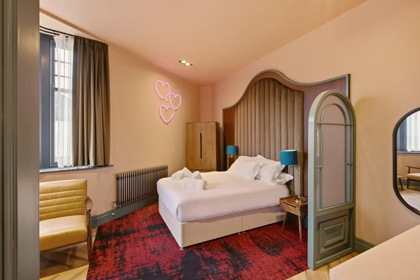 Open-plan sleeping area with double bed, bay window and neon wall light.