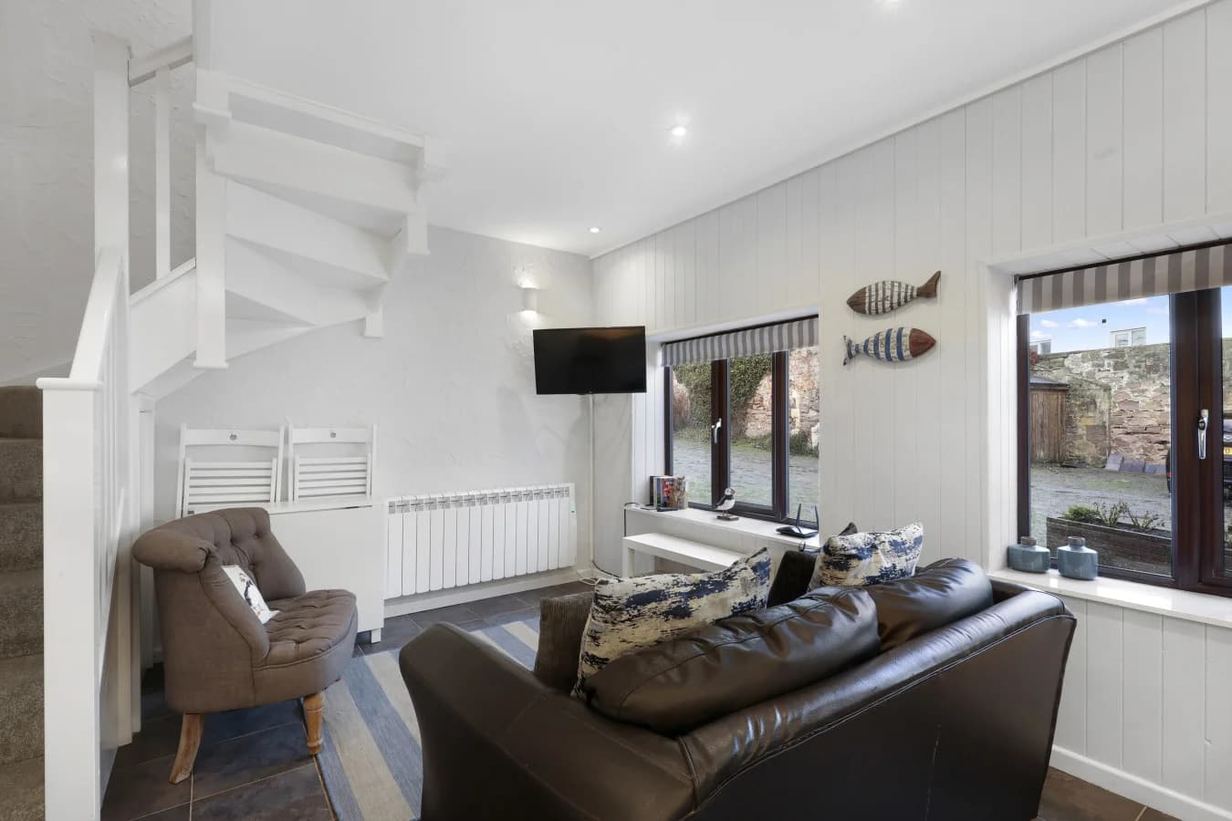 Open-plan living space with coastal tones, feature windows and TV