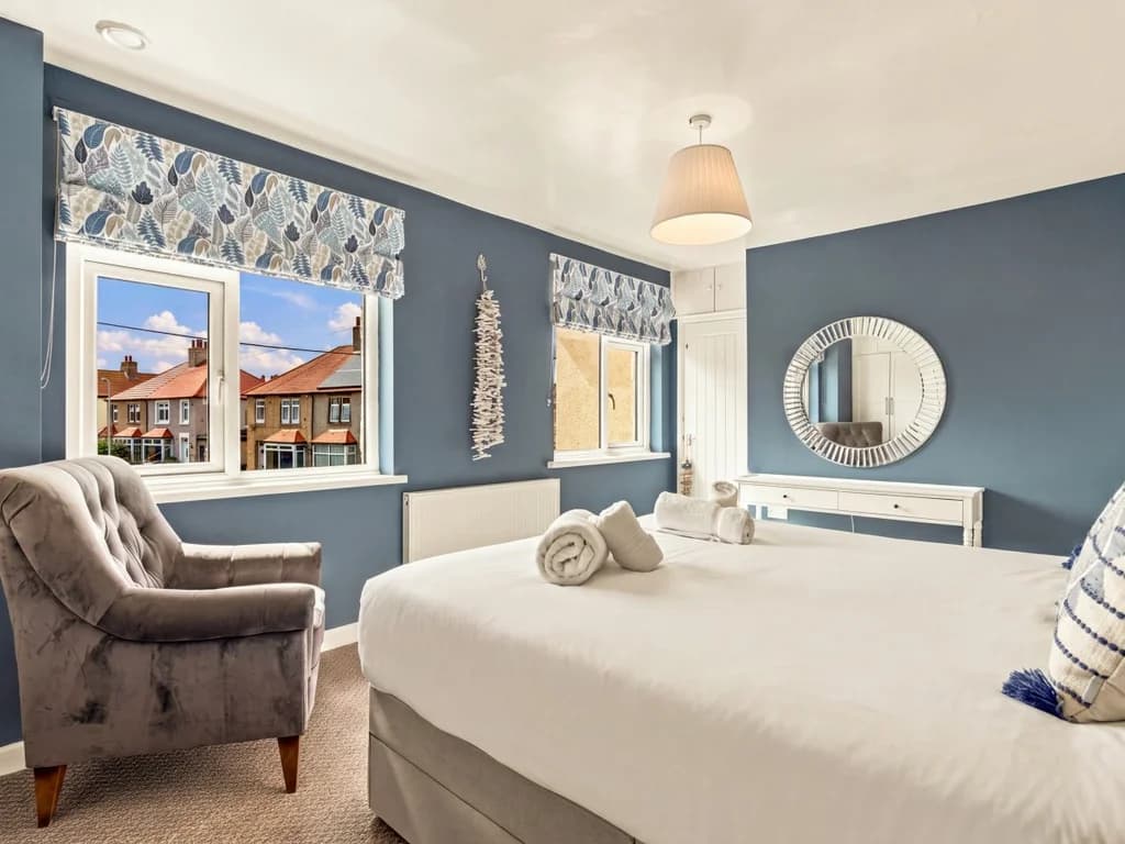 Spacious king bedroom with dressing table, armchair and twin windows.