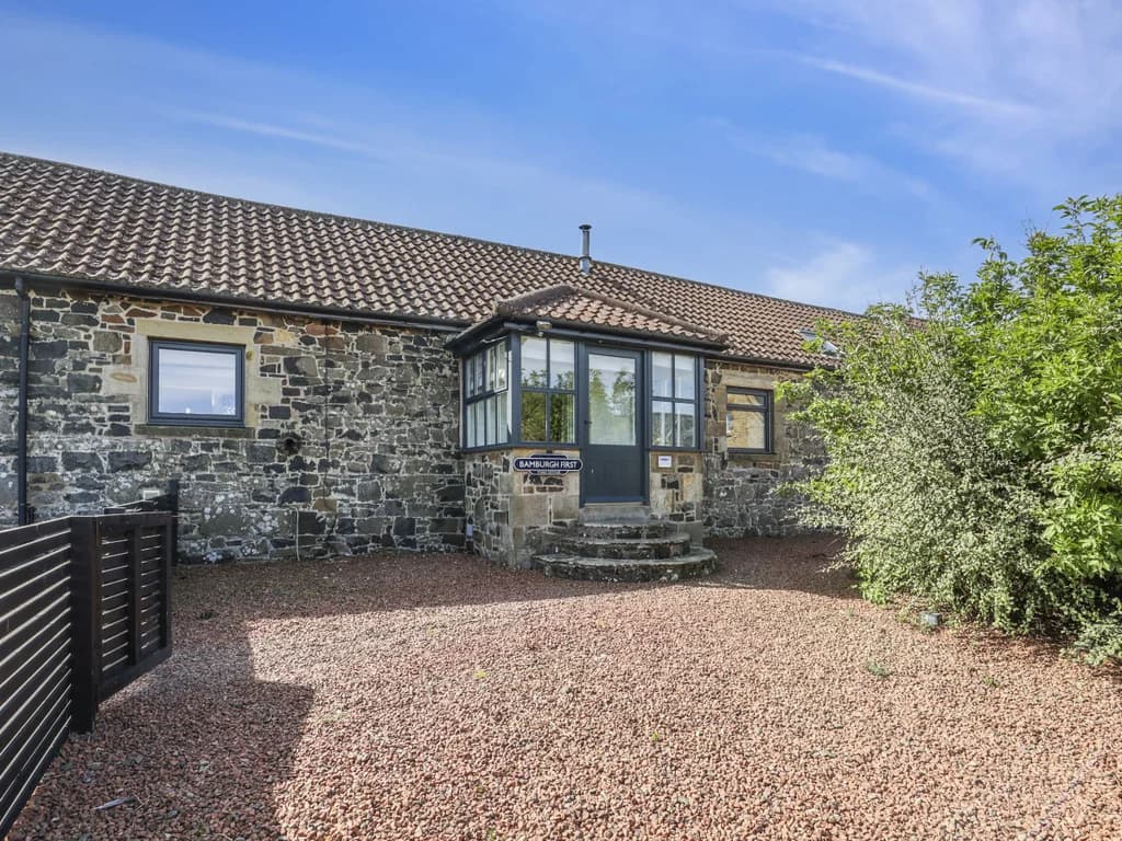 Exterior of sandstone stable cottage with gravel courtyard and bay window.
