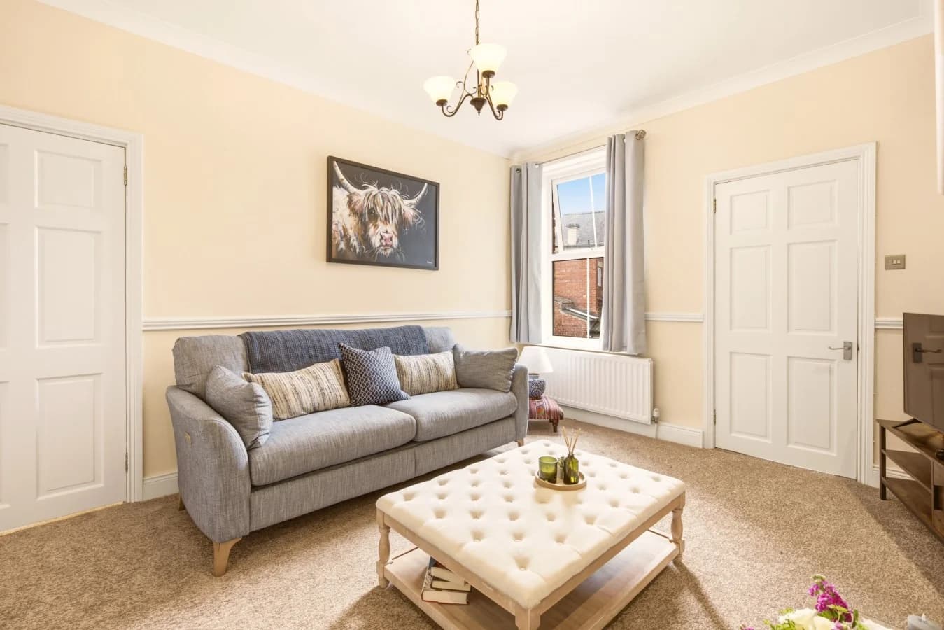 Living room with grey sofa, upholstered coffee table and Smart TV.