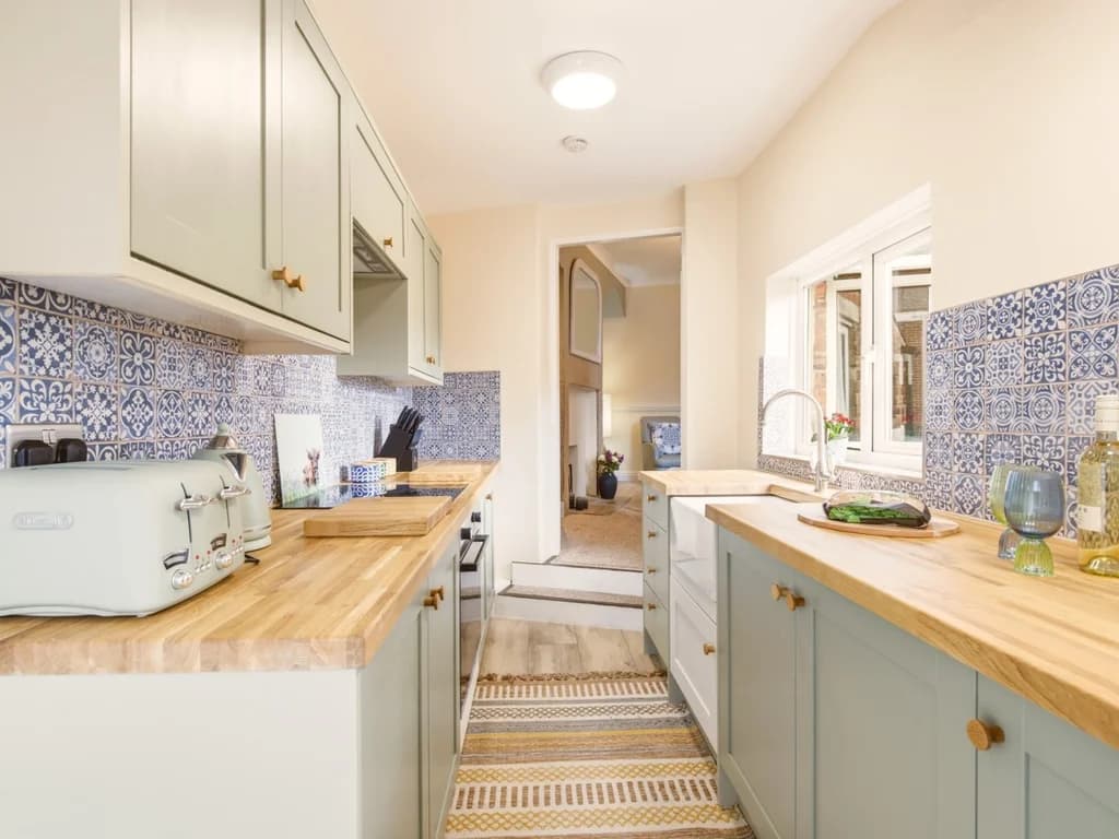 Galley kitchen with wooden worktops and blue patterned splashback.