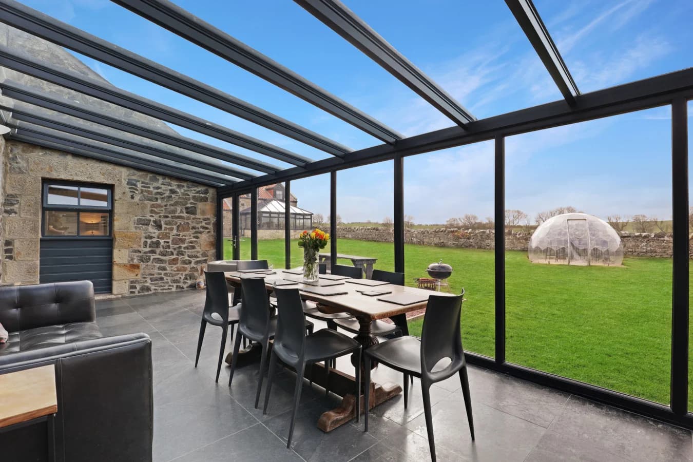 Conservatory dining area with glass walls overlooking enclosed lawn.