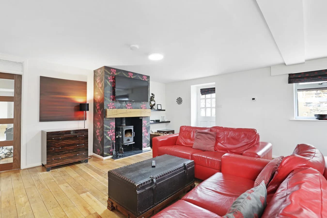 Open-plan lounge with red leather sofas and wood-burning stove.