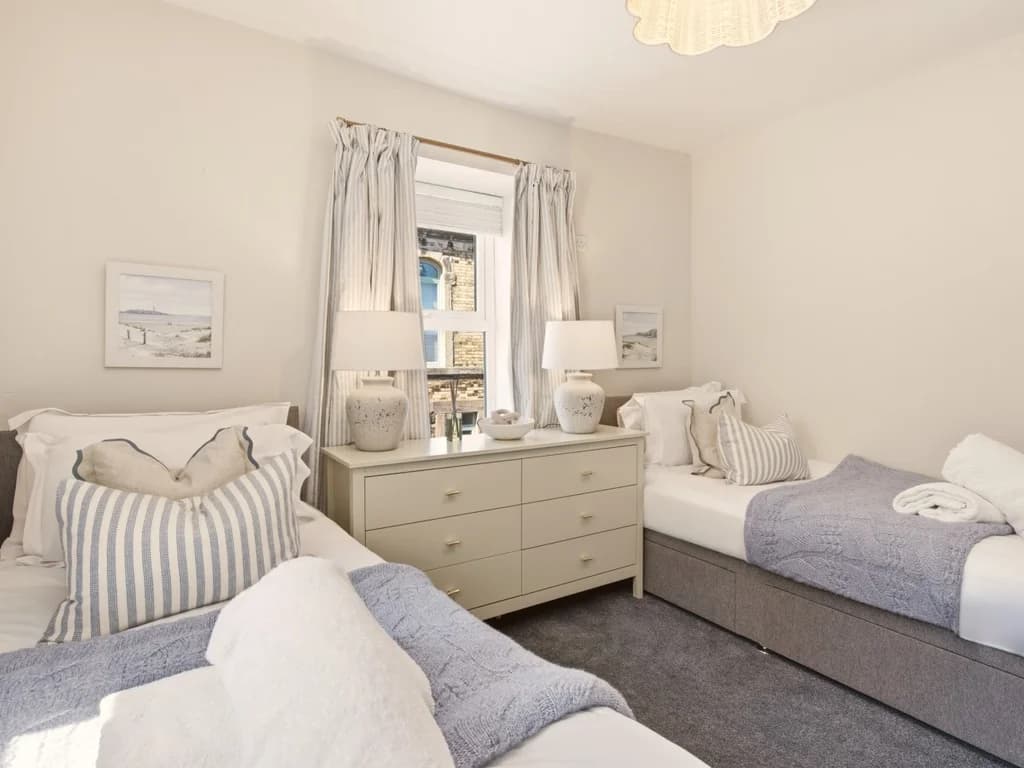 Twin bedroom with bedside chest, soft blue accents and natural light.